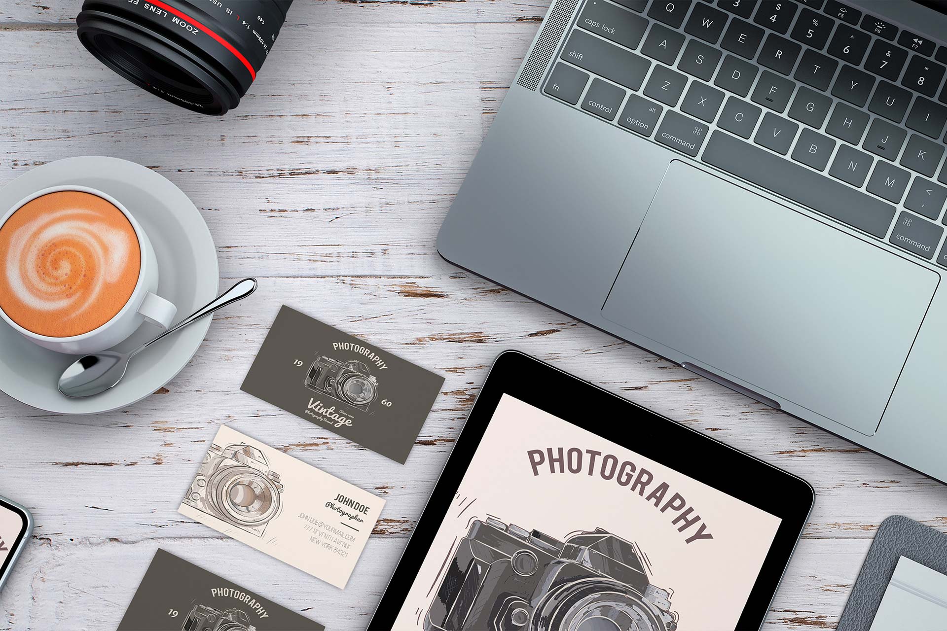 A desk that has a laptop, business cards of a photographer, a cup of coffee and an iPad.